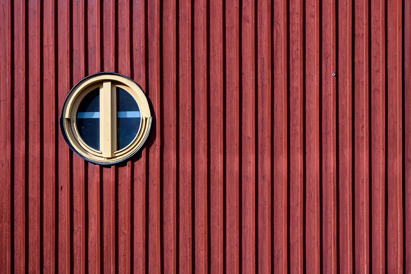 Farbige Holzfassaden für mehr Stil und Charme Eine Nahaufnahme einer röten Holzfassade mit einem gelben runden Fenster