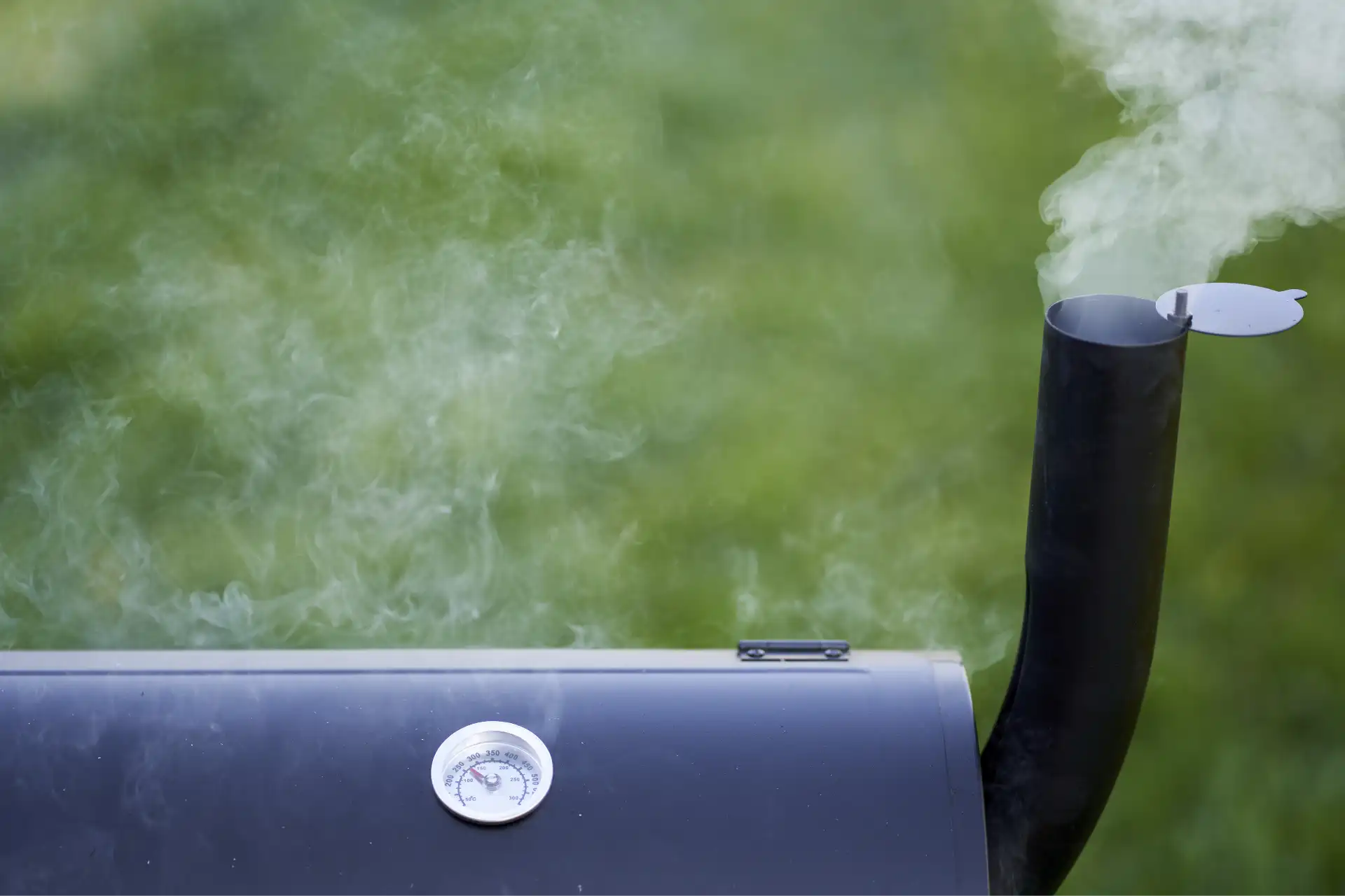 Oberer Teil eines schwarzen BBQ-Smokers mit Thermometer und aufsteigendem Rauch aus dem Kamin